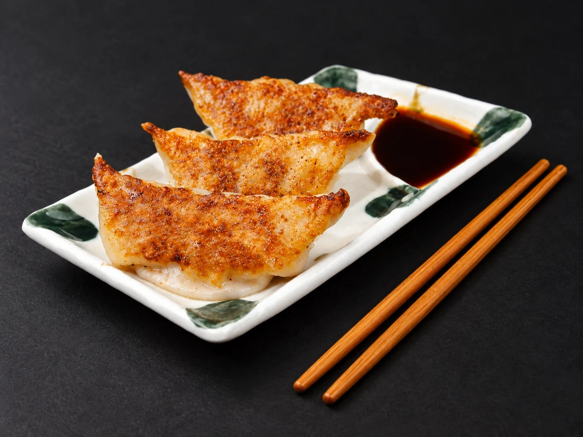 Three pork gyoza with golden, crispy bases on a ceramic plate